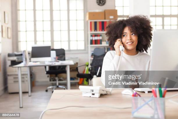 lächelnde assistentin mit festnetz-telefon im modernen büro - festnetzanschluss stock-fotos und bilder