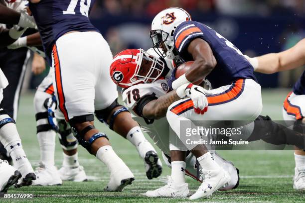 Kerryon Johnson of the Auburn Tigers pushes out of a tackle by Deandre Baker of the Georgia Bulldogs during the first half in the SEC Championship at...