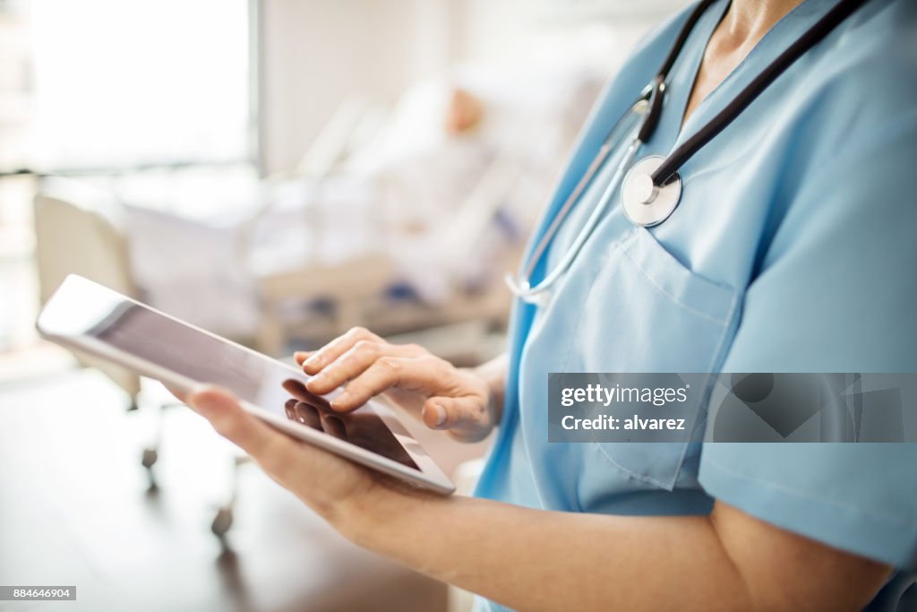 Midsection of nurse using tablet pc in hospital