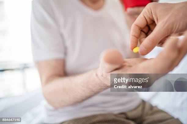 doctor's hand giving pills to senior man in ward - bed tablet stock pictures, royalty-free photos & images