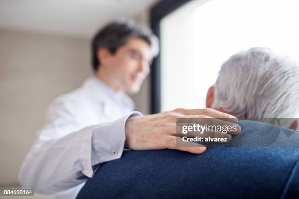 doctor keeping hand on senior man's back - weakness man stock pictures, royalty-free photos & images