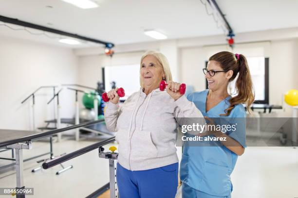 nurse helping senior woman in lifting dumbbells - rehabilitation center stock pictures, royalty-free photos & images