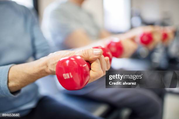 midsection of senior woman lifting dumbbells - rehabilitation center stock pictures, royalty-free photos & images