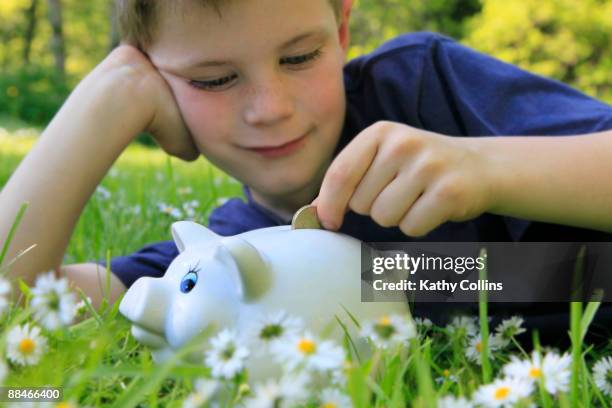 young boy seven years, putting money into piggy  - kathy cash stock pictures, royalty-free photos & images