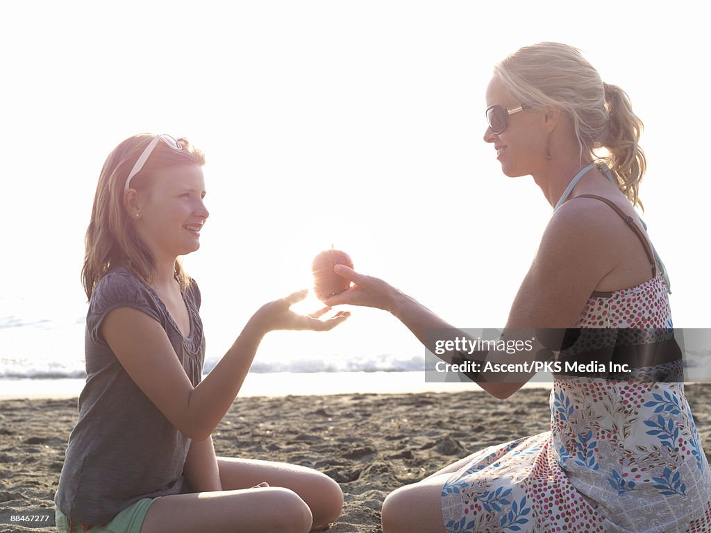 Mother and daughter share apple on beach