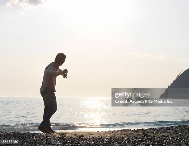 man skips stones across calm sea, sunset - throwing rocks stock pictures, royalty-free photos & images