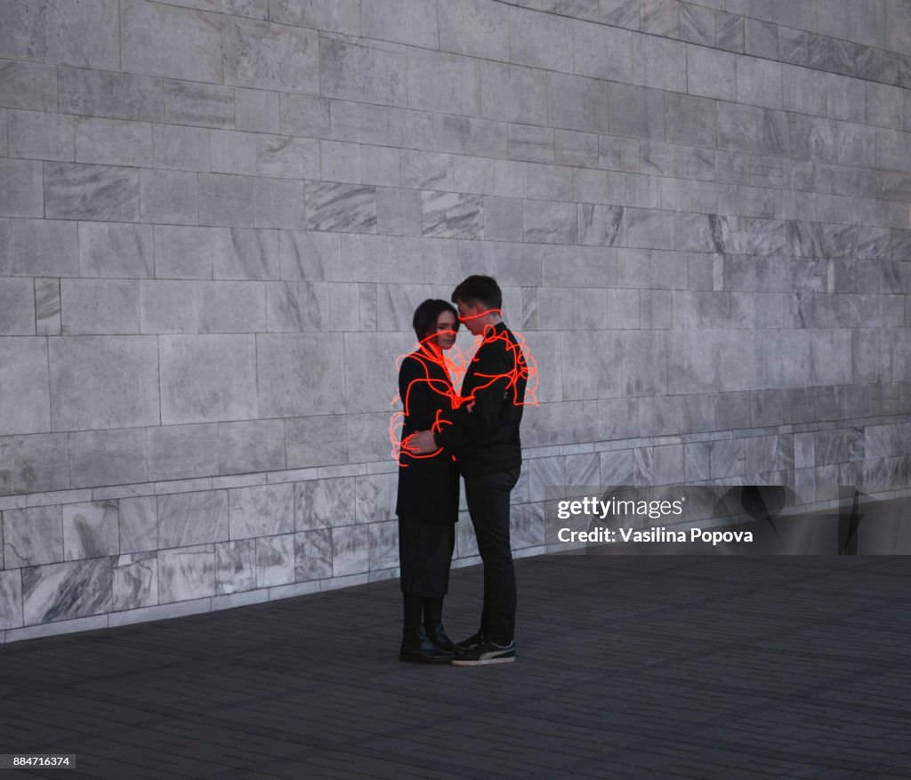 Man and woman entangled with neon wires against urban marble background