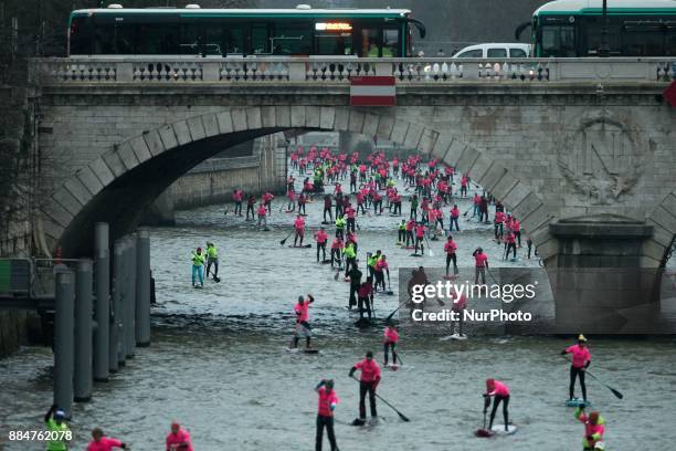 Paddle boarders pass near the Pont au Change bridge as they participate in the morning light in the Nautic SUP Paris crossing on the river Seine on...