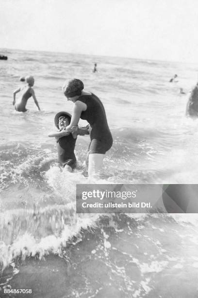 Badende am Strand, Mutter und Kind im Wasser, das Kind schreit