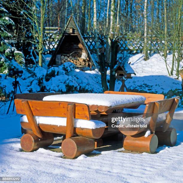 Rustikale Sitzgruppe mit Tisch aus Holz verschneit im winterlichen Garten