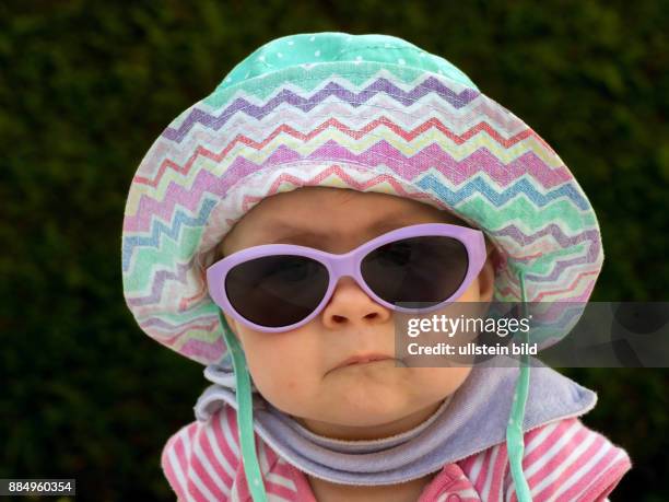 Ein Baby mit Sonnenbrille und Sonnenhut ist gut gegen die Hitze im Sommer ausgestattet