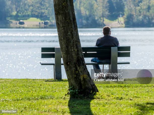 Auf einer Parkbank bei einem See sitzt einsam ein älterer Mann.
