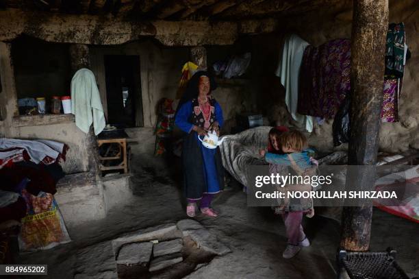 In this photograph taken on October 21, 2017 Afghan widow Janat Bibi holds a teapot walks inside her mud house in the remote village of Shemol in the...