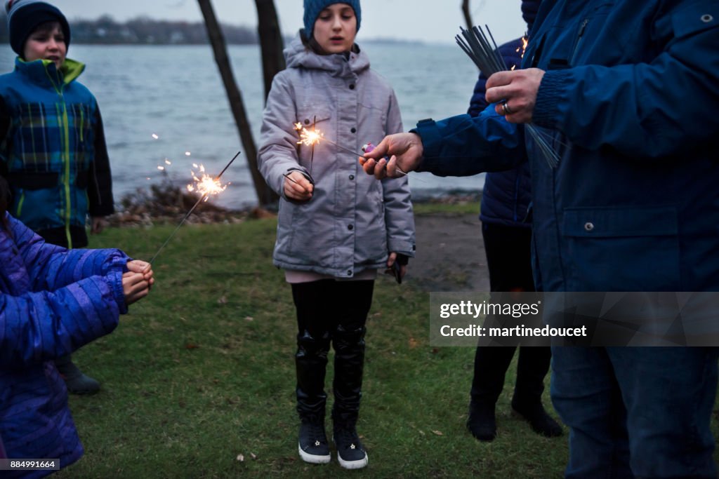 Amici e familiari festeggiano l'inverno con scintille all'aperto al crepuscolo