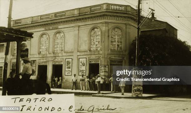 Group of men stand stand outside the Teatro Iriondo, Ciego de Avila, Cuba, 1943. Posters outside the cinema advertise 'La hermanita de su criado' ,...