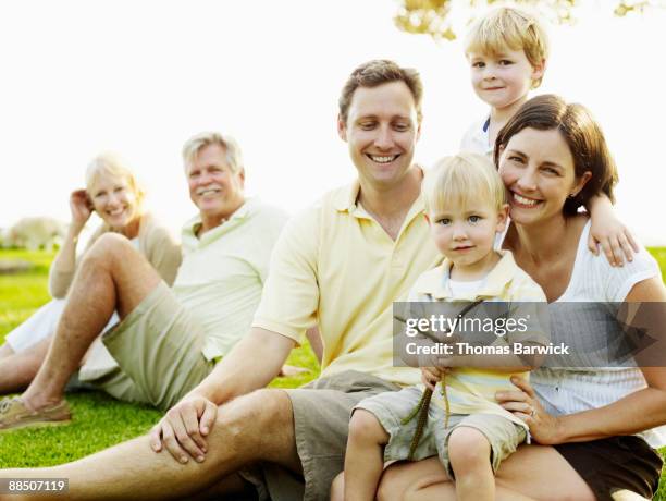 multi generational family sitting on grass - mutter grossmutter kind stock-fotos und bilder