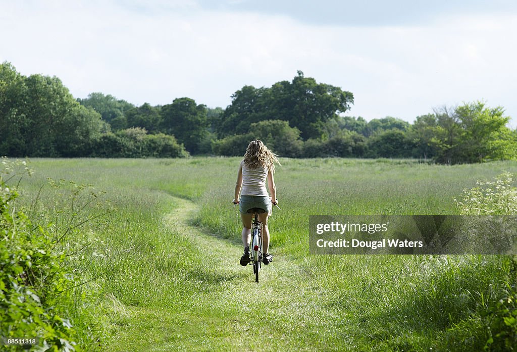 Young woman biking through countryside meadow.