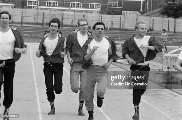 Group portrait of Dexys Midnight Runners with Kevin Rowland running at an athletics track in Birmingham, England in July 1981.