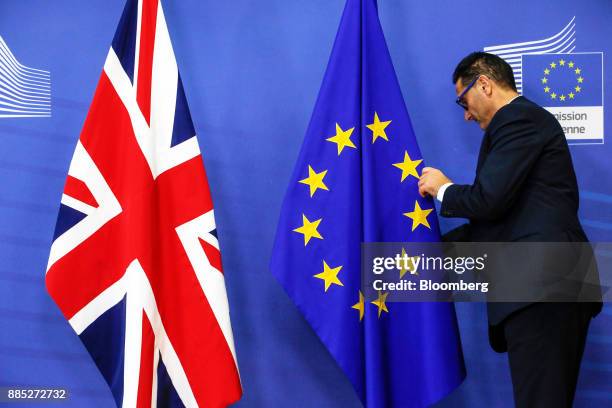 Worker adjusts a European Union flag as it stands next to a Union flag, also known as a Union Jack, right, inside the European Commission building in...