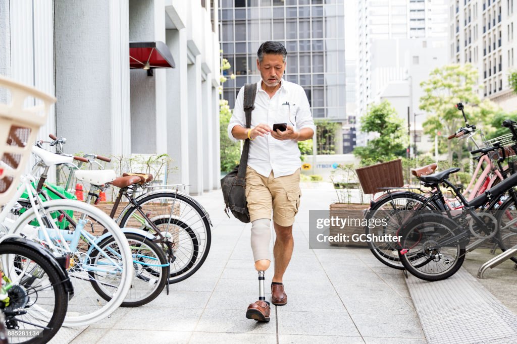 Japanse man met prothetische been wandelen langs de parkeerplaats terwijl het controleren van zijn telefoon