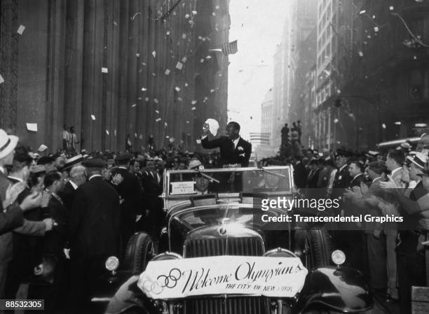 American athlete and Olympic gold medal winner Jesse Owens smiles as he waves at fans who line the streets during a ticker tape parade in honor of...