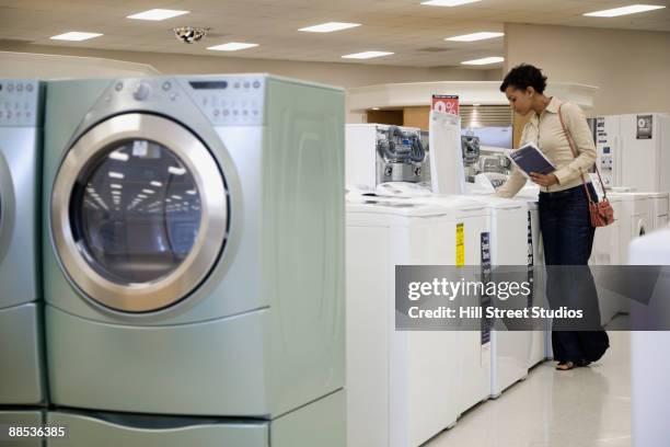 mixed race woman looking at washing machines in showroom - buying washing machine stock pictures, royalty-free photos & images