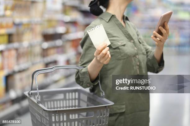 woman checking shopping list in supermarket - boodschappenlijst stockfoto's en -beelden