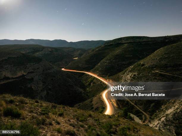 lights and trails of vehicles circulating along a road of mountain with curves closed in the night. valencian community, spain - car road imagens e fotografias de stock