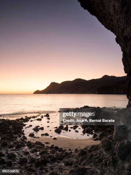 sunset  with nightfall light and the moon in the sky, on the beach and rocky coast of the cabo de gata with formations of volcanic rock. cabo de gata - nijar natural park, monsul creek, biosphere reserve, almeria,  andalusia, spain - mini moon 個照片及圖片檔