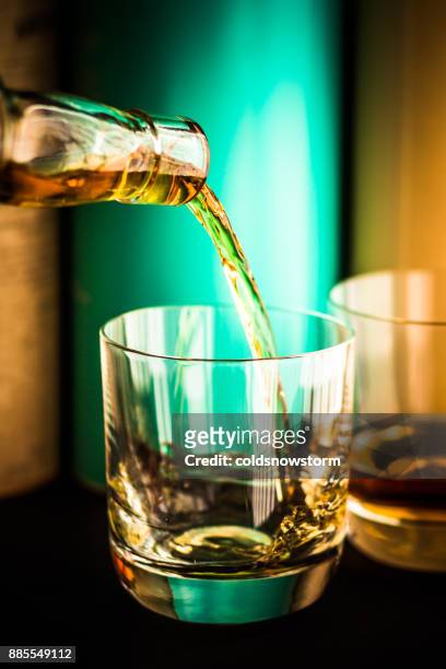 whisky being poured from clear glass bottle into glass tumbler with scotch malt whisky bottles in background - scotland distillery stock pictures, royalty-free photos & images