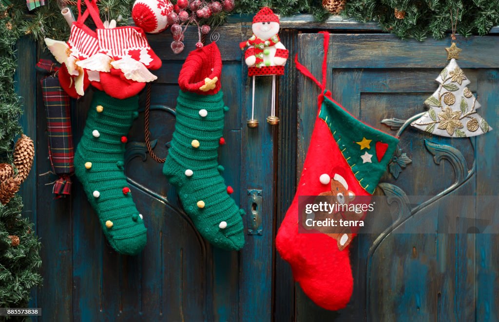 Red and green stockings, evergreen branch with pine cones and christmas toys on blue doors of old wardrobe.