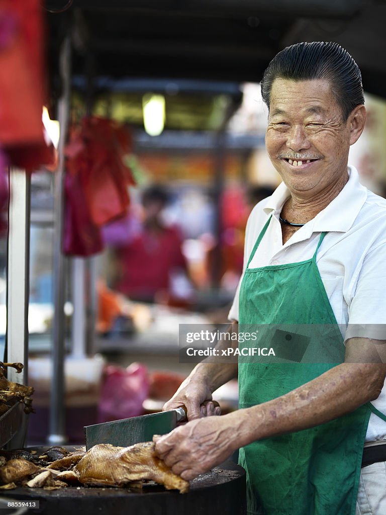 A smiling food vendor preparing duck.