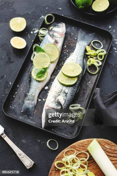 fresh sea bass with lemon and herbs ready for cooking on dark background. - dolphin fish fotografías e imágenes de stock