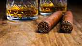 Two Cuban cigars with two glasses of whiskey on an old wooden table with a blurred background