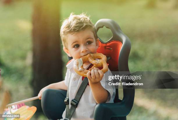 little boy eating a pretzel in a child seat on a bicycle. - baby eating toy stock pictures, royalty-free photos & images