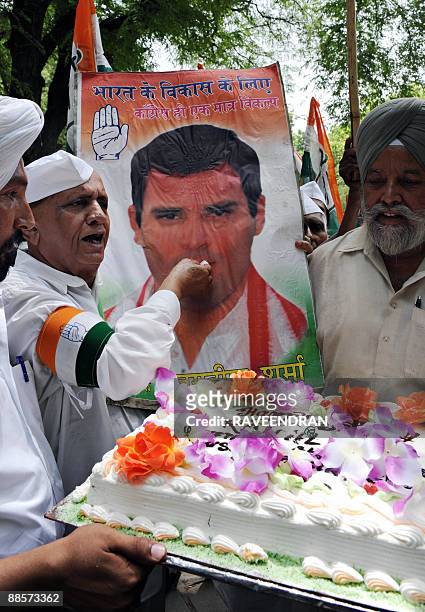 Congress Party supporter poses as he feeds cake to a banner bearing the portrait of Congress Party General Secretary Rahul Gandhi in celebration of...