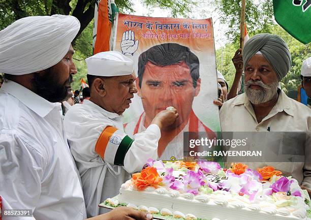 Congress Party supporter poses as he feeds cake to a banner bearing the portrait of Congress Party General Secretary Rahul Gandhi in celebration of...