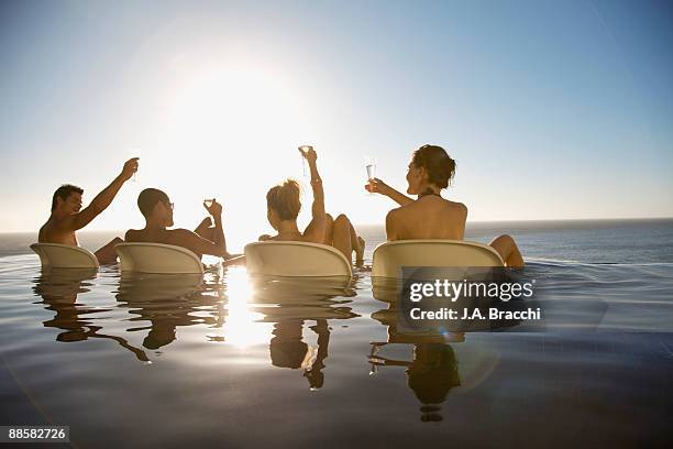 friends drinking in infinity pool near ocean - event horizon stock-fotos und bilder