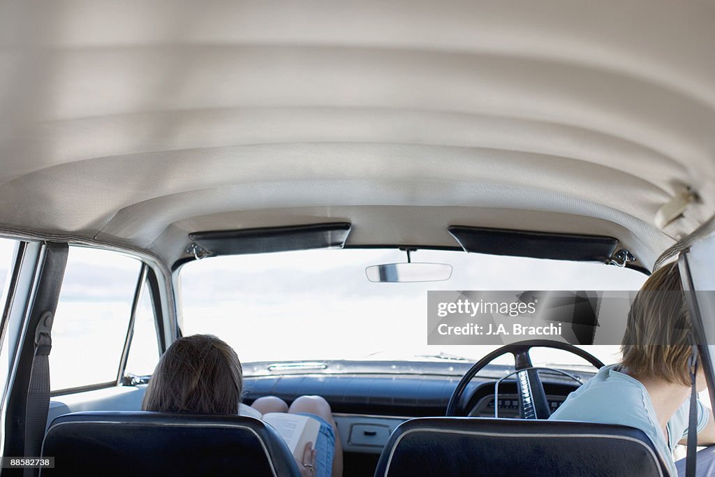 Woman reading in car while boyfriend looks out window