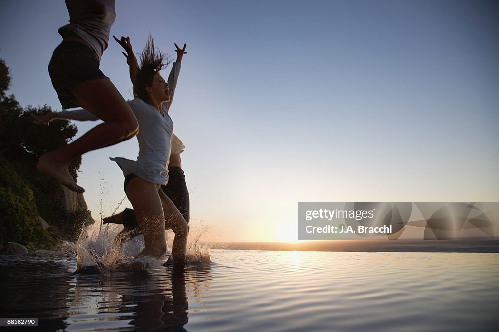 Friends jumping into infinity pool at sunset