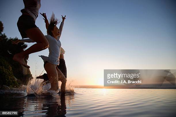 friends jumping into infinity pool at sunset - verlangen stockfoto's en -beelden