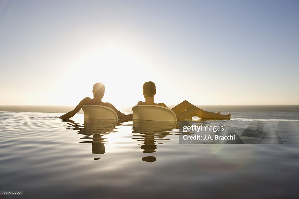 Friends soaking in infinity pool near ocean
