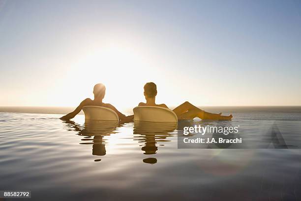 friends soaking in infinity pool near ocean - women sunbathing pool - fotografias e filmes do acervo