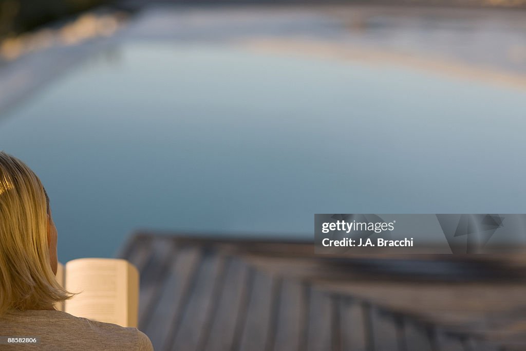 Woman reading on deck near swimming pool