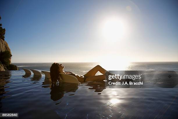 woman soaking in infinity pool near ocean - women sunbathing pool - fotografias e filmes do acervo