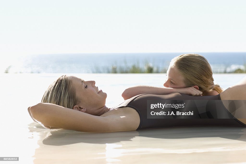 Mother and daughter laying in swimming pool