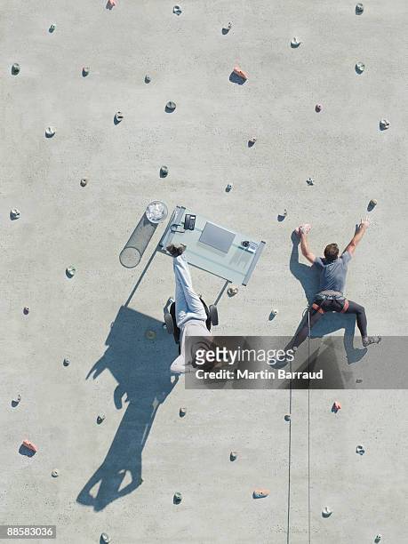businessman and desk on rock climbing wall - sport extreme stock-fotos und bilder