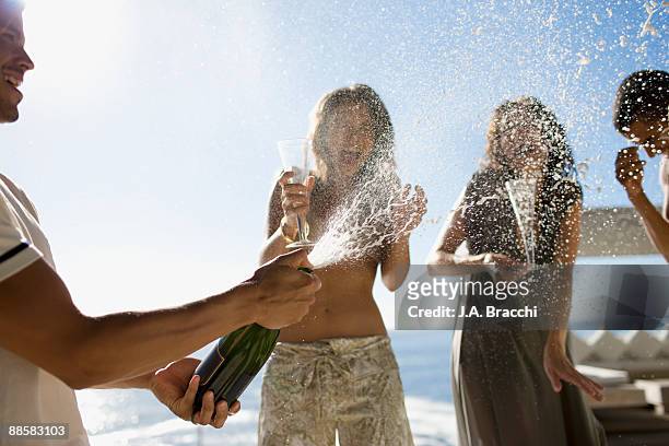 man squirting friends with champagne - sparkling wine stockfoto's en -beelden