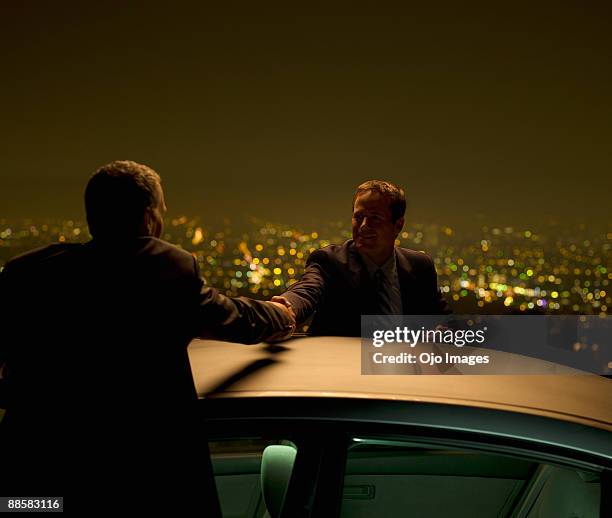 businessmen shaking hands at city overlook at night - secret handshake stock pictures, royalty-free photos & images