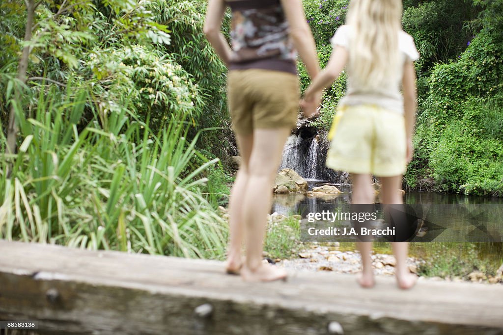 Mother and daughter holding hands near remote stream